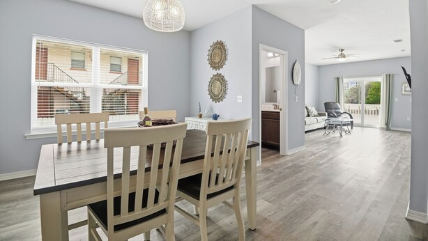 A dining area with a wooden table and chairs, a chandelier, and a view of a building with windows and a staircase. - Lux Ft Walton Beachfront Home MINS to HCA Florida Hospital/ Sleeps 4/ King Bed (Fort Walton Beach)