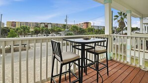 A covered outdoor seating area with a table and chairs, overlooking a street with buildings and palm trees. - Lux Ft Walton Beachfront Home MINS to HCA Florida Hospital/ Sleeps 4/ King Bed (Fort Walton Beach)