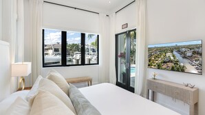 A hotel room with a large bed, a view of a marina, a TV mounted on the wall, and a console table with decorative items. - The Rendez-Vous Villa (Fort Lauderdale)