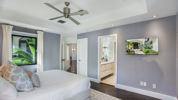 A bedroom with a bed, a ceiling fan, a window with curtains, and a hallway leading to a bathroom. - The Rendez-Vous Villa (Fort Lauderdale)