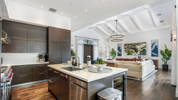 A modern kitchen with a central island, stainless steel appliances, and a dining area with a sofa and a view of the outdoors. - The Rendez-Vous Villa (Fort Lauderdale)