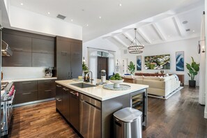 Una cocina moderna con una isla central, electrodomésticos de acero inoxidable y un comedor con sofá y vistas al exterior.