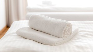 Cama bem arrumada com duas toalhas brancas dobradas.
