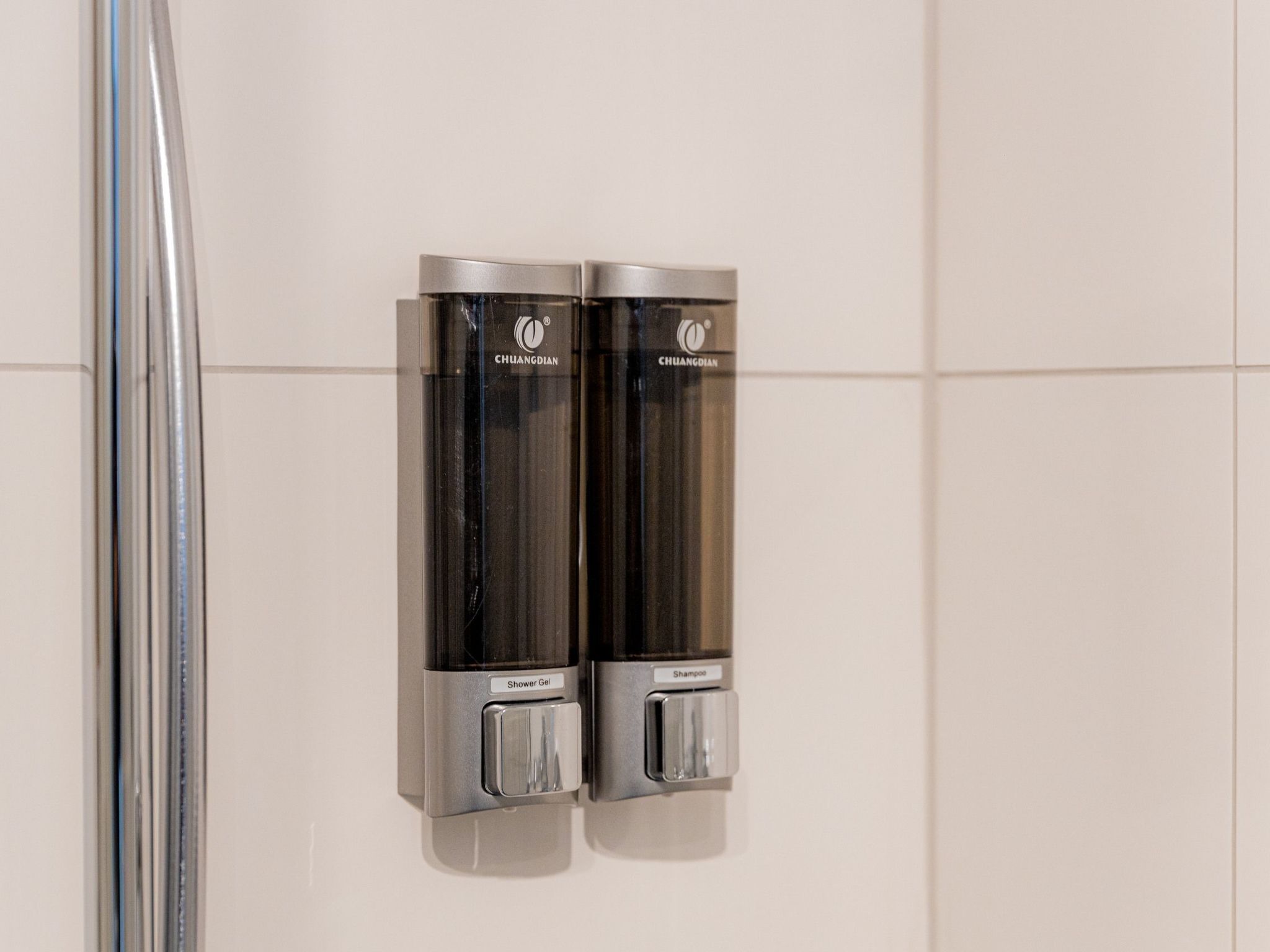 A wall-mounted dispenser with a label for 'Shower Gel' and another for 'Shampoo'.