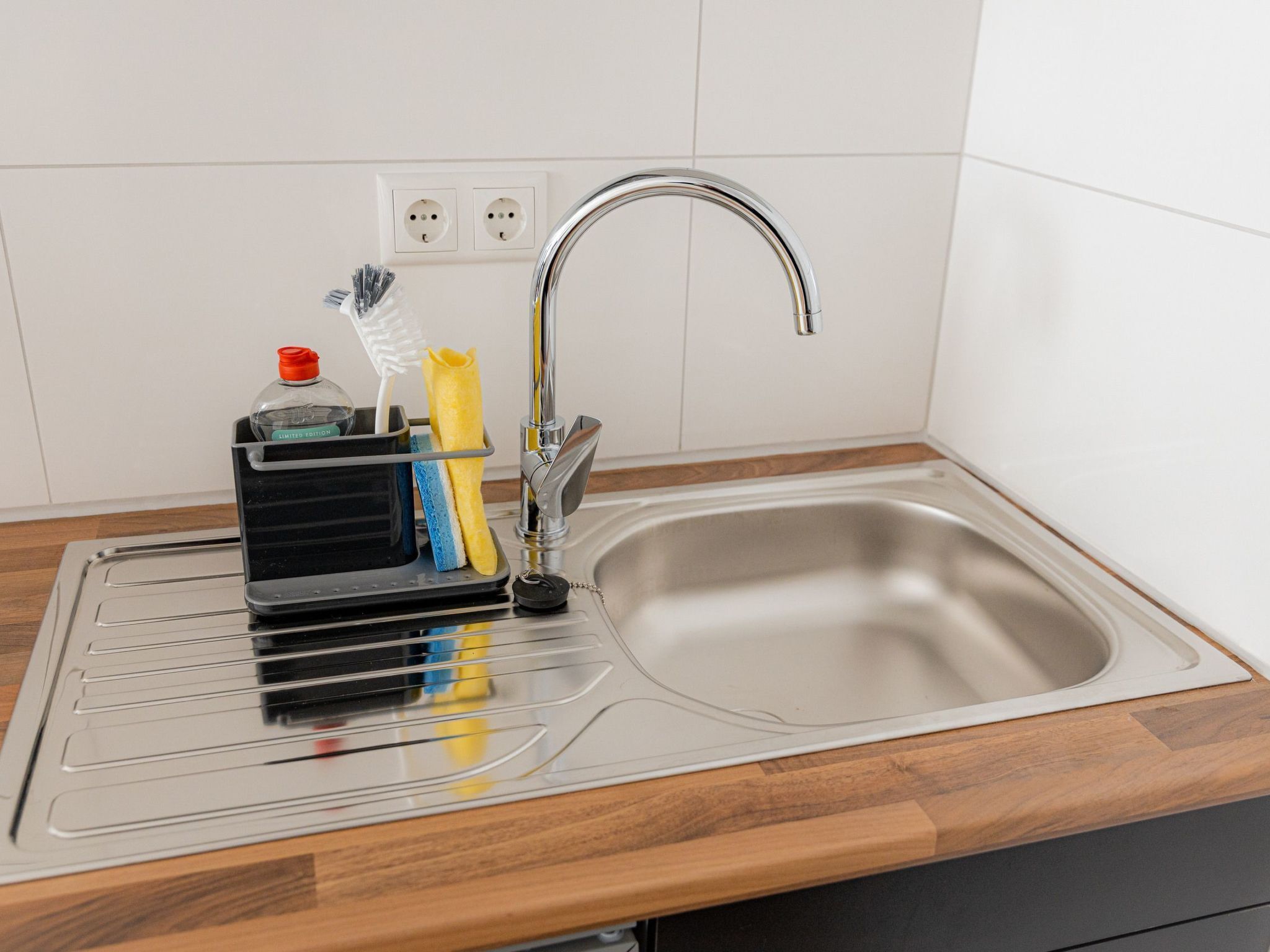 A stainless steel kitchen sink with a faucet, a soap dispenser, and a sponge holder on the countertop.