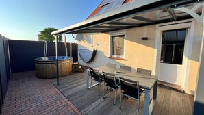 Een overdekt buitengebied met een jacuzzi, een tafel met stoelen en een dak met zonnepanelen.
