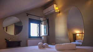 Hotelkamer met een bed, een ronde spiegel, een raam met gordijnen, een airconditioning en een wandlamp.