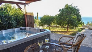 Een bubbelbad met twee glazen witte wijn op een tafel, omringd door rieten stoelen, met uitzicht op zee en begroeiing.
