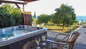 A hot tub with two glasses of white wine on a table, surrounded by wicker chairs, with a view of the sea and greenery. - Villa Harmony with jacuzzi, in Lourdata of Kefalonia. (Lourdata)