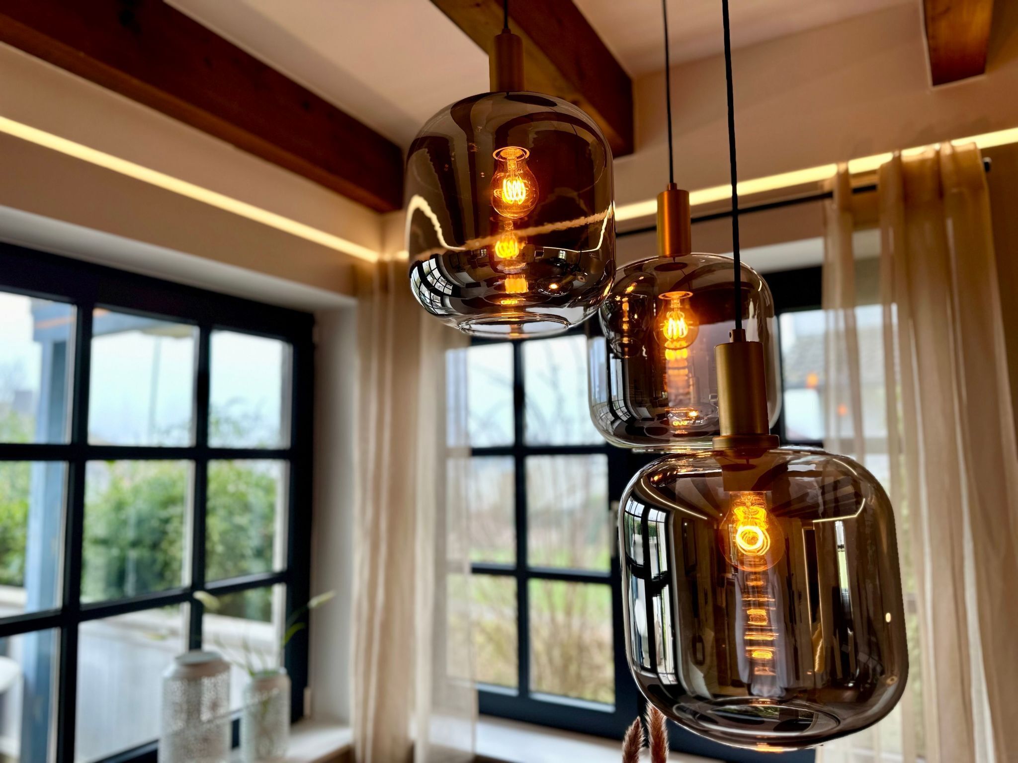 A modern interior with a large window, a hanging light fixture, and a wooden ceiling beam.