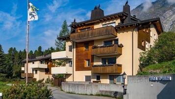Un edificio a più piani con facciata in legno, balconi e montagne sullo sfondo.