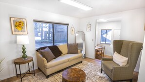 Een woonkamer met een bank, fauteuil, rond bijzettafeltje en een klein tafeltje met een lamp. Er is een groot raam met uitzicht.