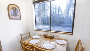 Een eettafel met vier stoelen, een raam met uitzicht op bomen en een hek, en een lijst met een afbeelding aan de muur.