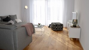 Un soggiorno moderno con un divano grigio, un tavolino da caffè, un pouf bianco e nero, una lampada da terra e una TV su un mobile bianco.