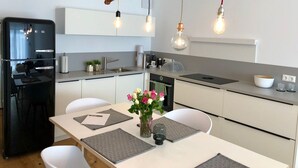 Una cucina moderna con un frigorifero nero, mobili bianchi, un tavolo da pranzo con sottopiatti e una lampada a sospensione realizzata con un ramo.