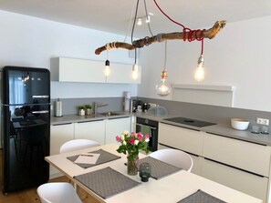 Eine moderne Küche mit einem schwarzen Kühlschrank, weißen Schränken, einem Esstisch mit Platzsets und einer Lampenleuchte aus einem Ast.