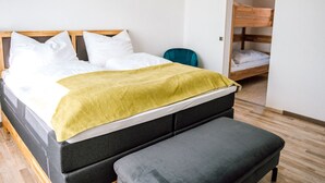 Une chambre à coucher bien rangée, avec un lit, un banc et, au fond, un lit superposé.