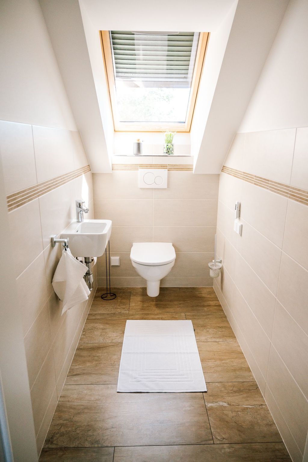 Et lille, smalt badeværelse med ovenlys, toilet, håndvask og et lille vindue.