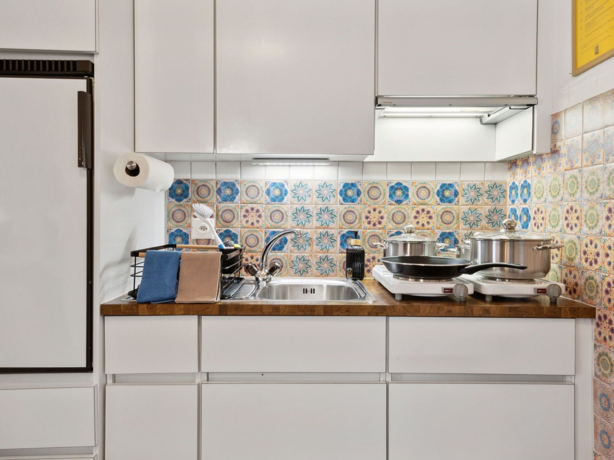 A kitchen with white cabinets, a sink, a stove, and colorful tile backsplash.