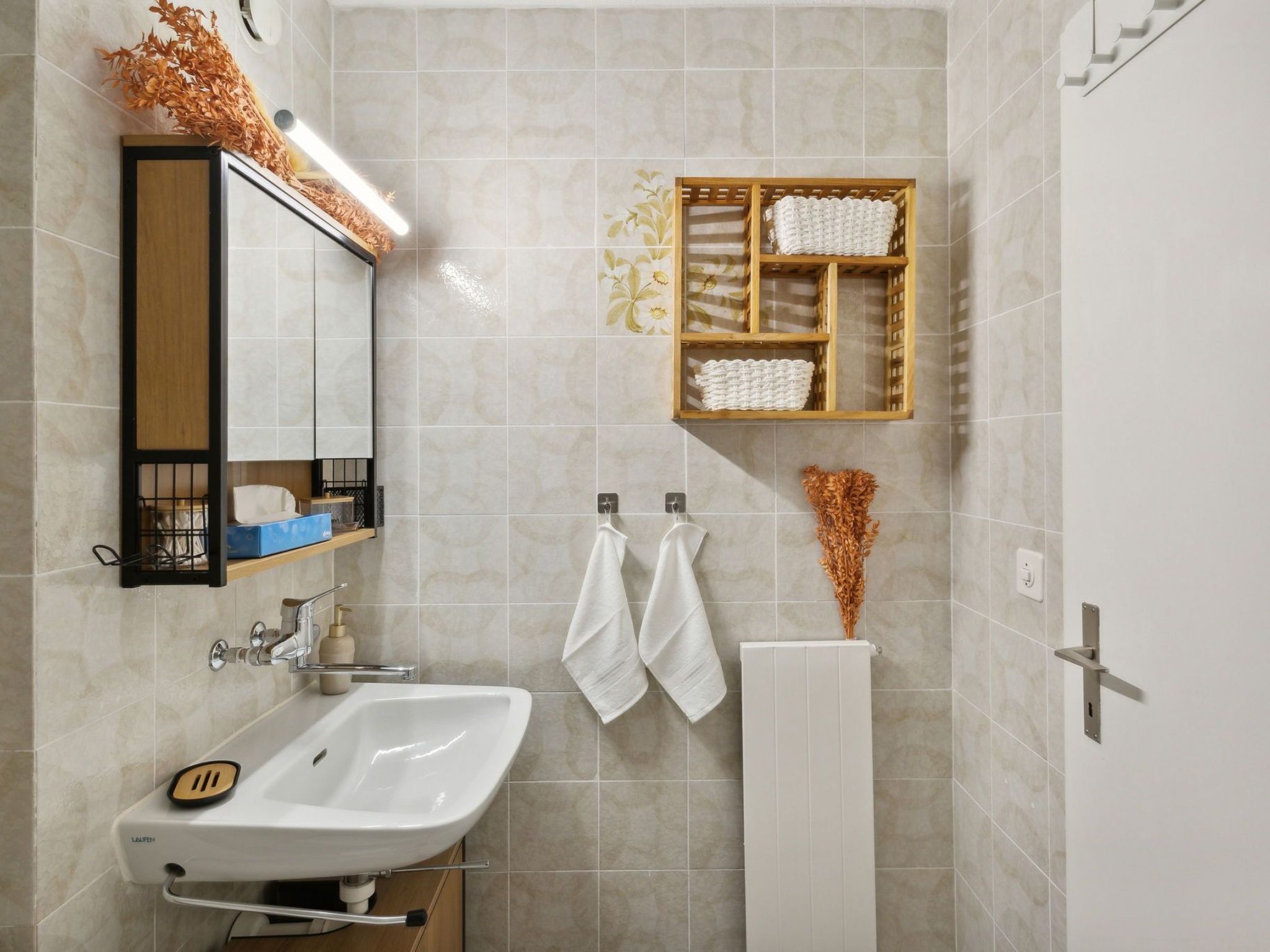 Un baño con lavamanos blanco, un espejo, toallero y repisa con toallas.