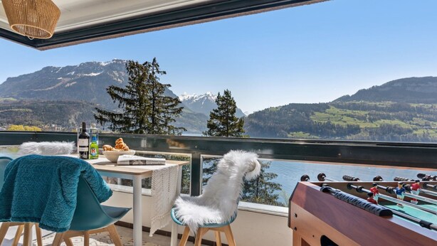 A balcony with a view of mountains, a foosball table, and a table with drinks and pastries.
