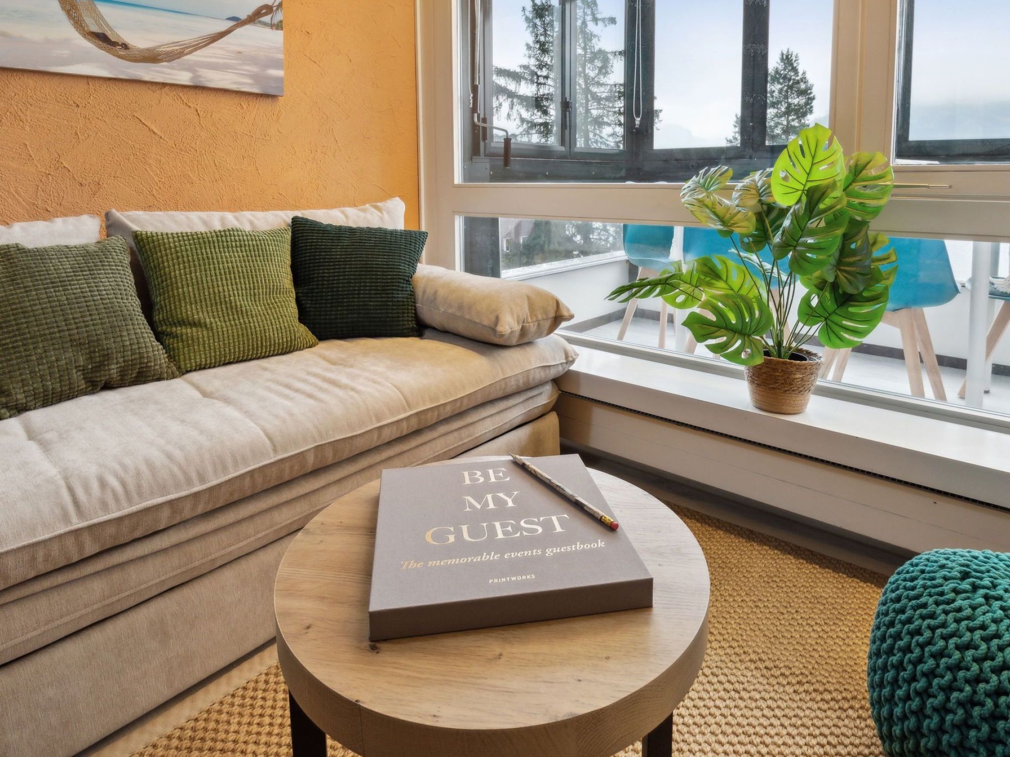 Una sala de estar acogedora con un sofá color crema, una mesa redonda de madera y un ventanal con vistas a árboles.