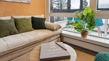 Una sala de estar acogedora con un sofá color crema, una mesa redonda de madera y un ventanal con vistas a árboles.