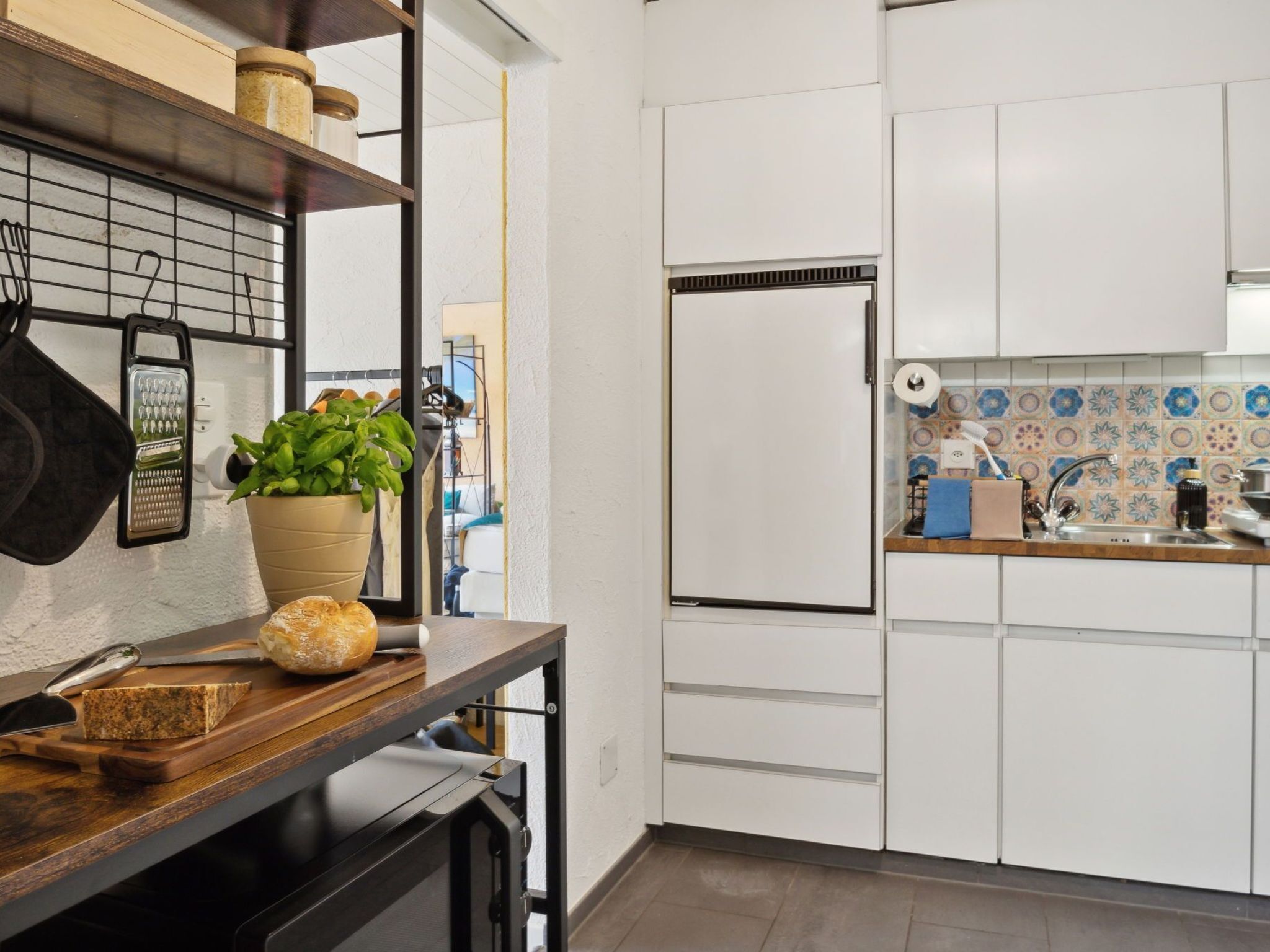 Una cocina moderna con armarios blancos, un refrigerador empotrado, una encimera de madera y una planta en maceta.