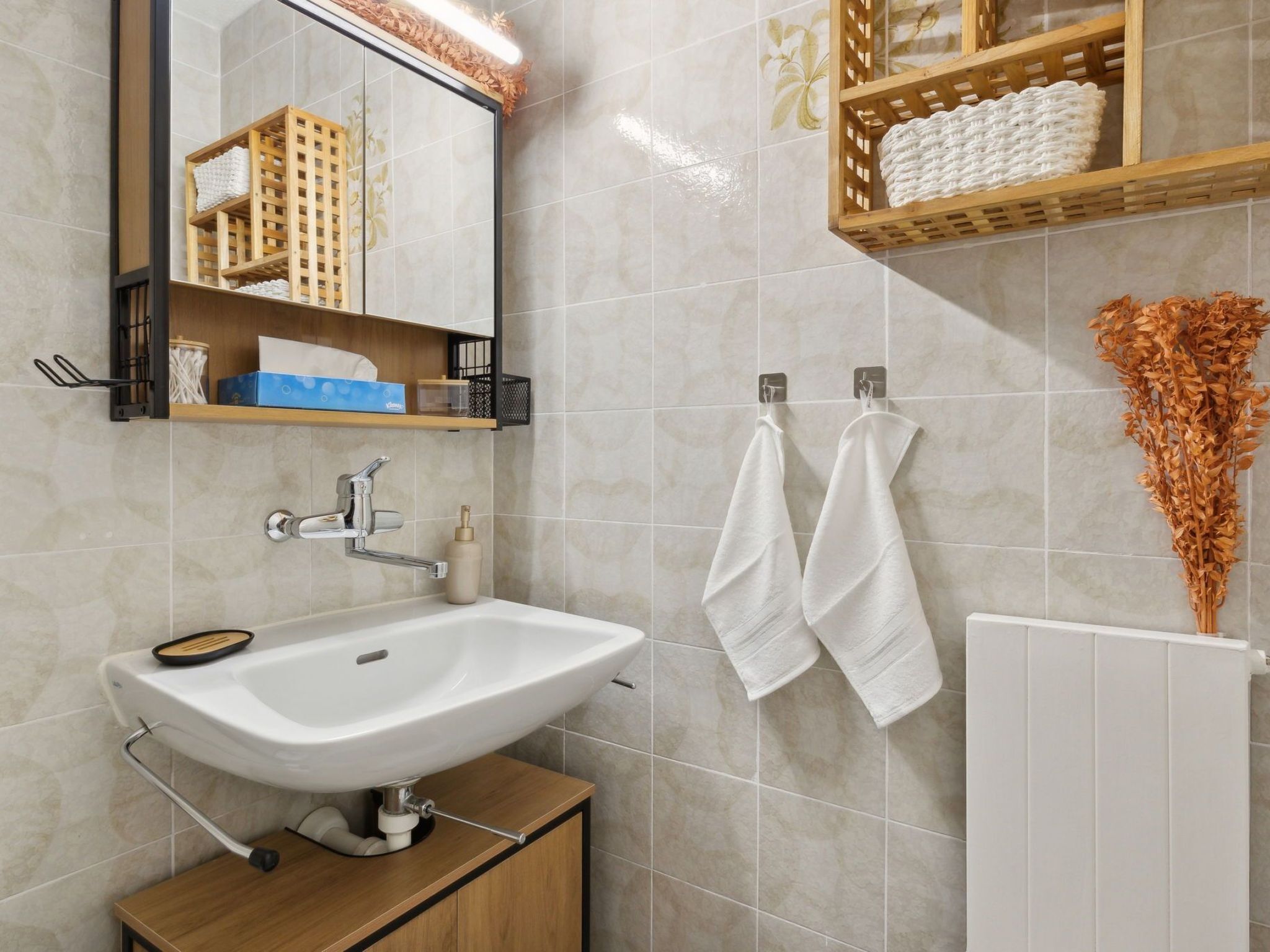 Un baño con lavamanos blanco, armario de madera, espejo y barra para toallas.