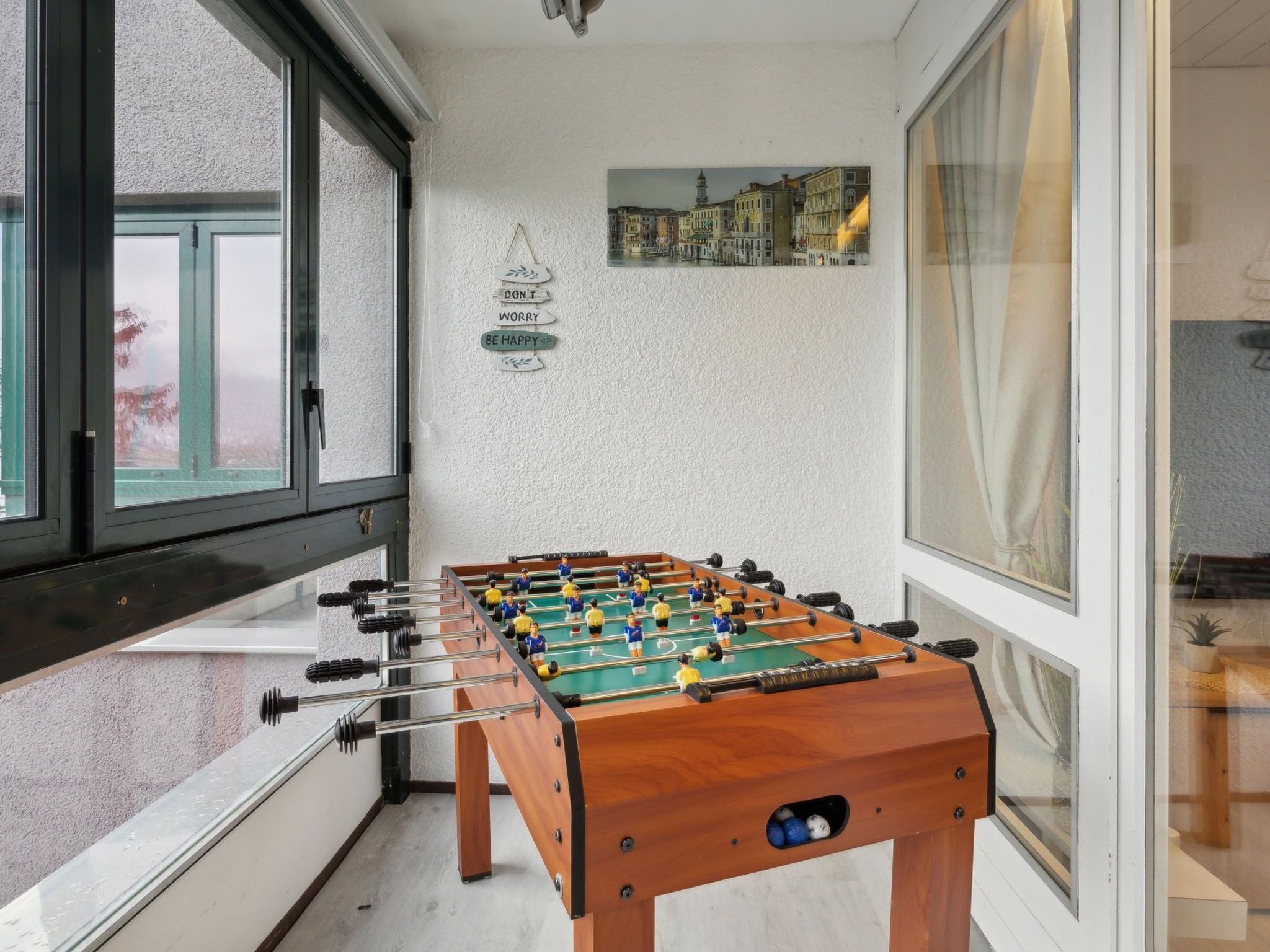 A foosball table in a room with a large window, a cityscape painting, and motivational wall art.