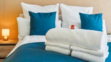 A neatly made bed with white and blue bedding, a red decorative item on the pillows, and a lamp on the nightstand.