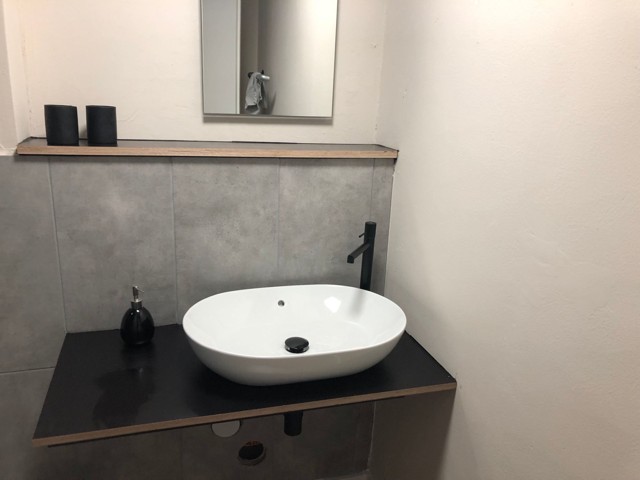 Un bagno moderno con un lavandino bianco, un rubinetto nero e una piccola bottiglia di sapone su un ripiano nero.