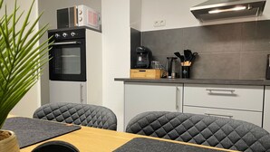 Una cucina moderna con forno integrato, macchina del caffè e microonde. Sono presenti due sedie dal design trapuntato e un tavolo in legno.