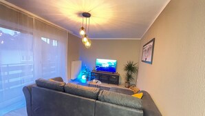 Un soggiorno con un ampio divano grigio, una televisione a schermo piatto, un lampadario a soffitto e una pianta in vaso.