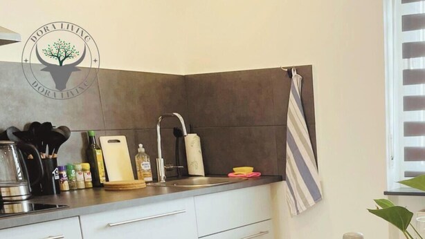 Una cucina moderna con mobili bianchi, uno schienale scuro e un asciugamano a righe appeso al muro.