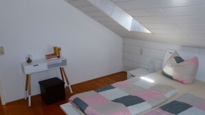 A bedroom with a sloped ceiling, a desk, a bed with a quilt, and a pillow. - ApartmentmitAusblick by Interhome (Wörth)
