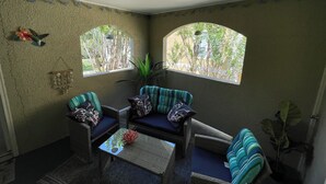 Quarto de canto com duas janelas em arco, mobiliário de vime e uma mesa pequena.