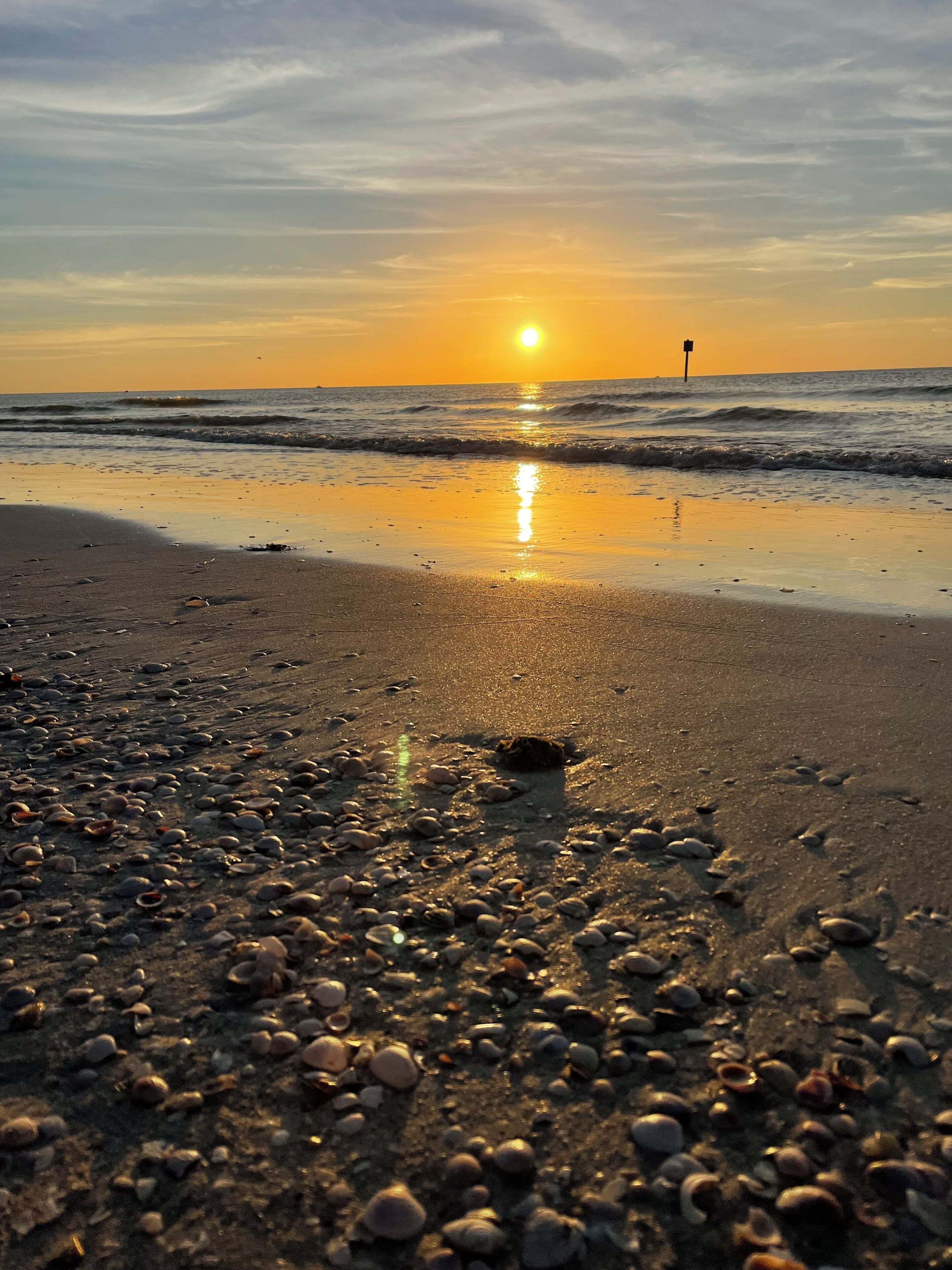 A beach with pebbles and a sunset in the background.