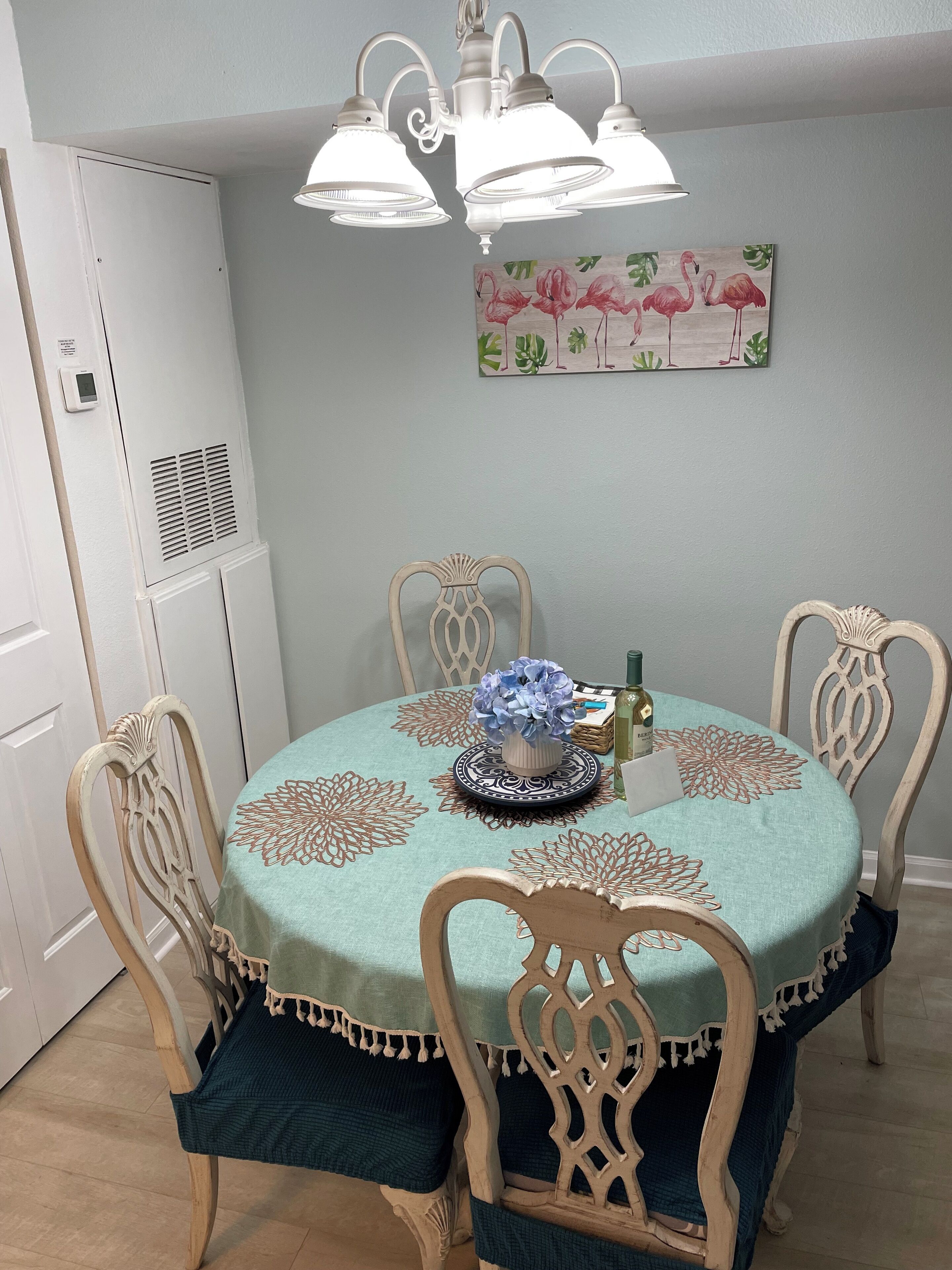 Zona pranzo con tavolo rotondo, quattro sedie, un lampadario, condizionatore d'aria a parete e un quadro con fiori.