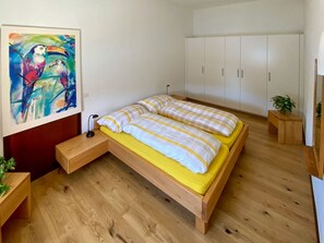 A bedroom with a wooden bed, a nightstand, a wall-mounted lamp, a wardrobe, and a painting. - Villa Egeria by Interhome (Brissago)