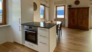 Moderni keittiö, jossa on valkoiset kaapit, sisäänrakennettu uuni ja musta työtaso. Ikkunasta avautuu näkymä ulos, ja oikealla puolella on puinen kaappi.