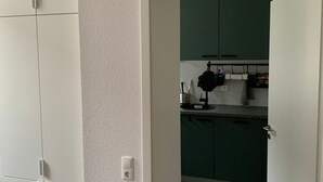 Una stanza con un armadio bianco, una cucina con mobili verdi e una porta bianca.