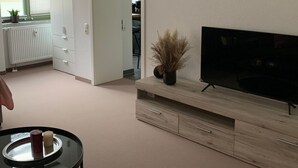 Un soggiorno moderno con una TV a schermo piatto, un mobile TV in legno, un tavolino con una candela e un divano.