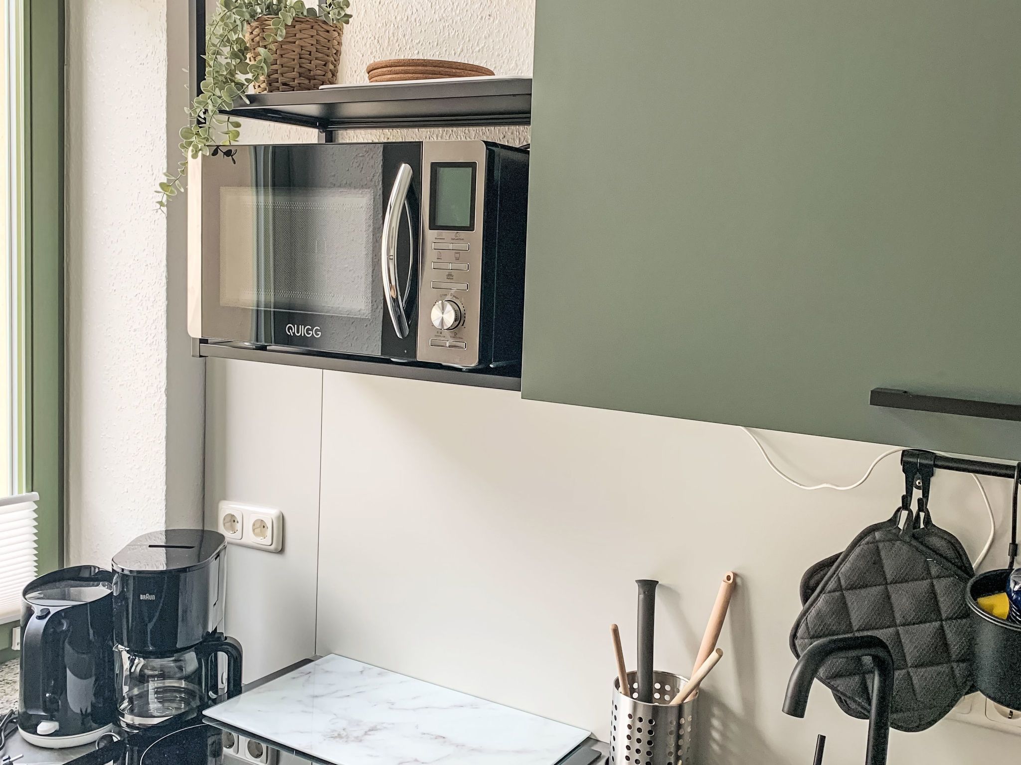 Une cuisine compacte équipée d’un four à micro-ondes encastré, d’une machine à café et d’une bouilloire posées sur le plan de travail.