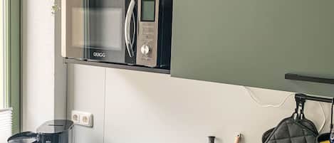 A compact kitchen with a built-in microwave, a coffee maker, and a kettle on the counter.