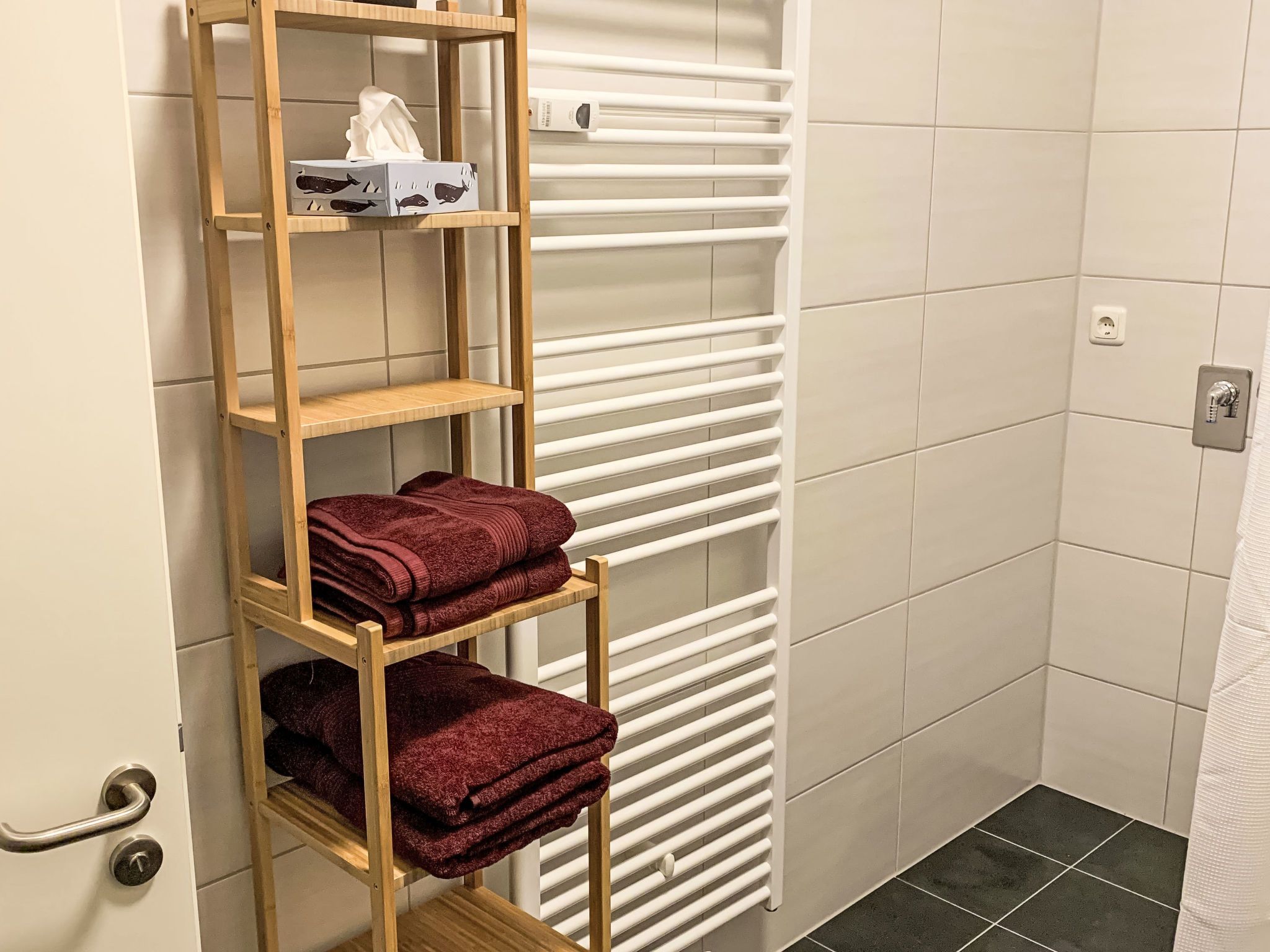 A bathroom with a wooden shelf holding towels and a box of tissues.
