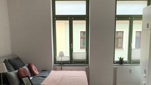 Una camera da letto moderna con un letto, un tavolino con vassoio, una poltrona e due finestre vista edifici.