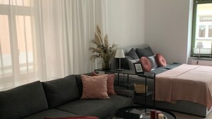 Un soggiorno moderno con un divano grigio, un tavolino rotondo e un letto con coperta rosa.