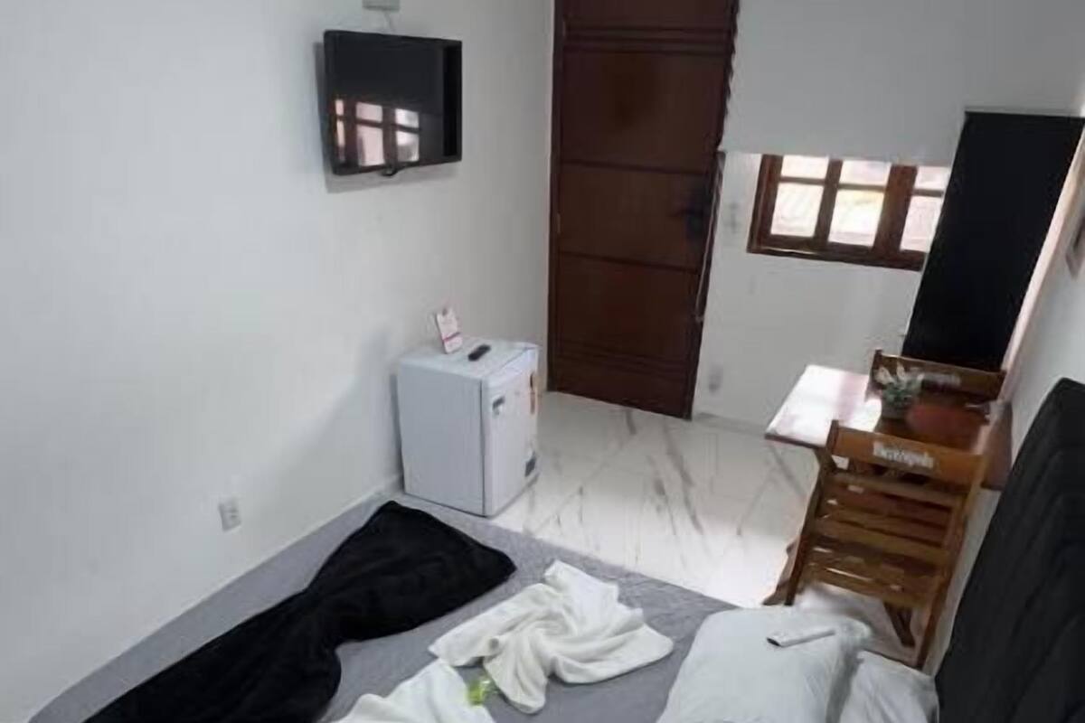 A bedroom with a bed, a desk, a chair, a wardrobe, and a small heater.