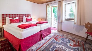 Un dormitorio con cabecera a cuadros, dos camas con ropa de cama roja, un tapete estampado y una ventana con cortinas.